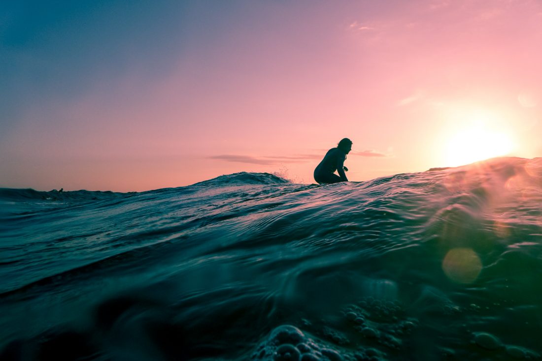 A surfer paddles out into the sunset 