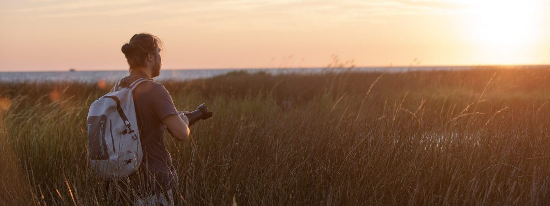 Picture of photographer in a marsh wearing an essential travel accessory, the Patagonia storm front backpack