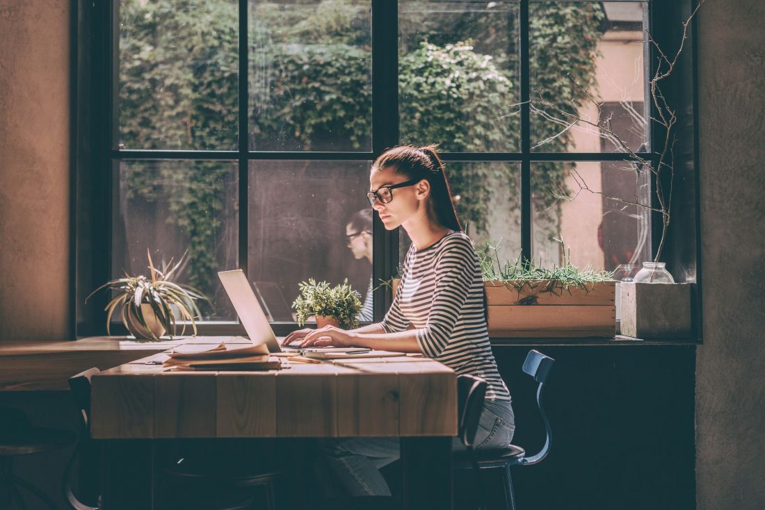 Picture of a woman blogging on her laptop by a window